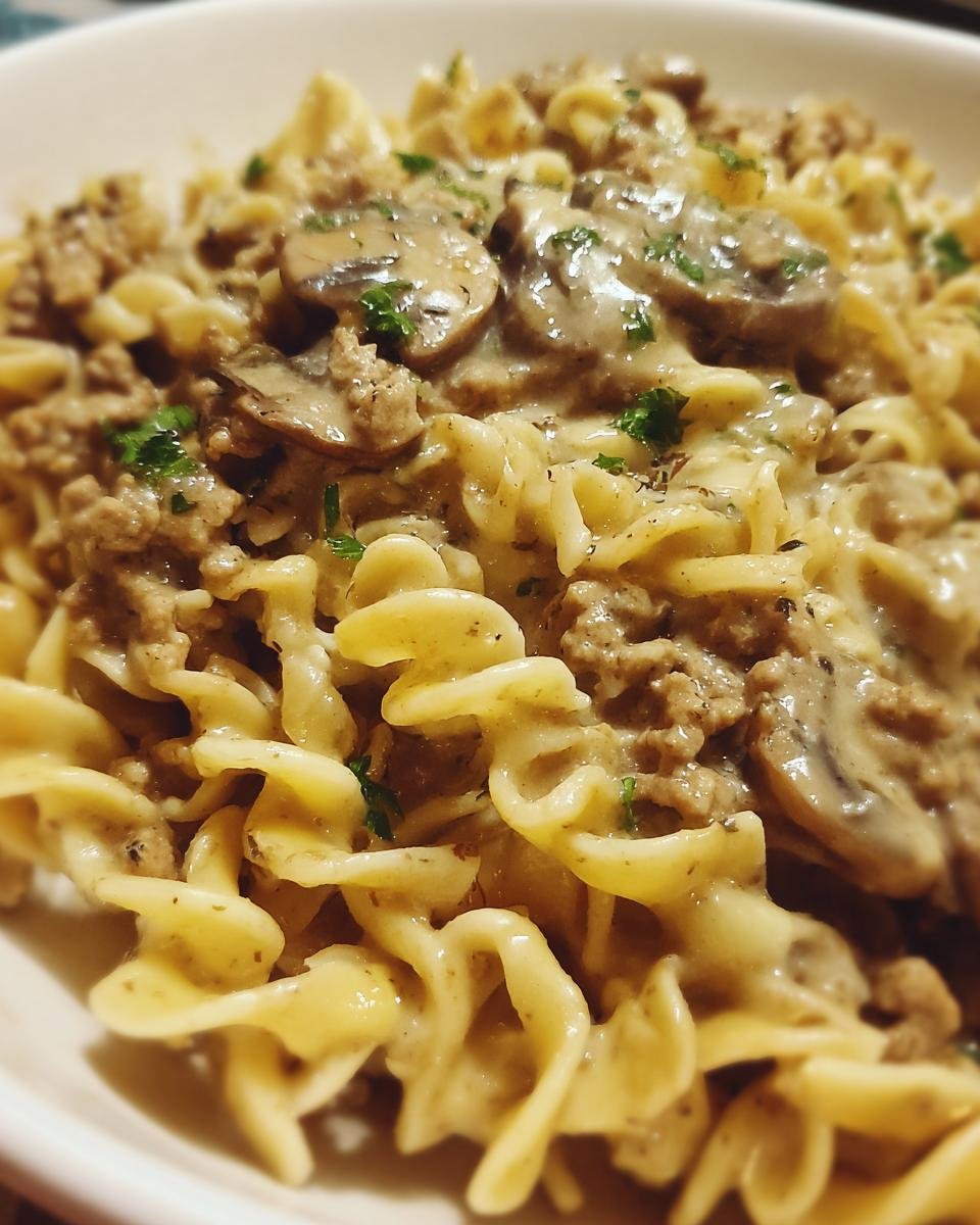 A close-up shot of a bowl of Creamy Turkey Stroganoff served over wide egg noodles, topped with mushrooms and parsley.