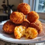 A stack of golden brown Crispy Fried Cheese Balls, with one broken open showing melted, stringy cheese inside.