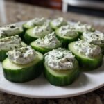 A white plate filled with freshly made Dilly Cucumber Bites topped with creamy dill spread.