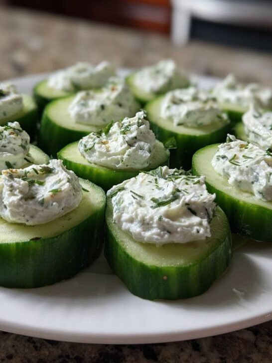 A white plate filled with freshly made Dilly Cucumber Bites topped with creamy dill spread.