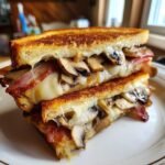 A close-up of a halved Double Bacon Swiss Mushroom Melt sandwich overflowing with melted Swiss cheese, bacon, and saut&eacute;ed mushrooms.
