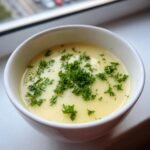 A close-up of a bowl of creamy French Garlic Soup, topped generously with fresh chopped parsley.