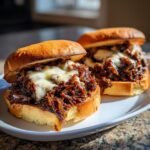 Two open-faced French Onion Beef Sloppy Joes topped with caramelized onions and melted white cheese on toasted buns.