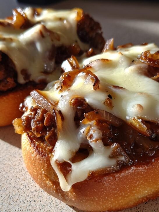 Two open-faced French Onion Beef Sloppy Joes topped with caramelized onions and melted white cheese.