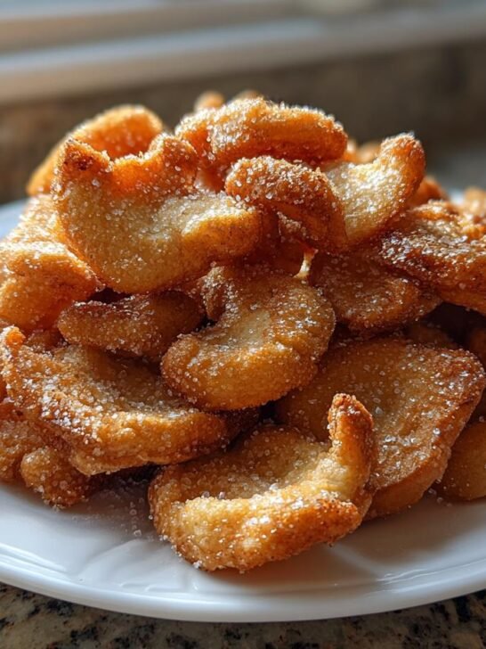 A pile of golden brown, sugar-dusted fried mushrooms served on a white plate.
