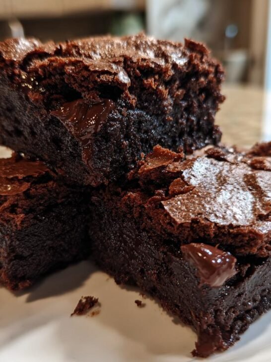 Three rich, dark, fudgy chewy browkies stacked on a white plate, showing gooey chocolate chips.