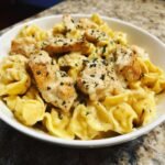 Close-up of Garlic Butter Chicken Alfredo Tortellini pasta topped with seasoned chicken pieces in a creamy sauce.