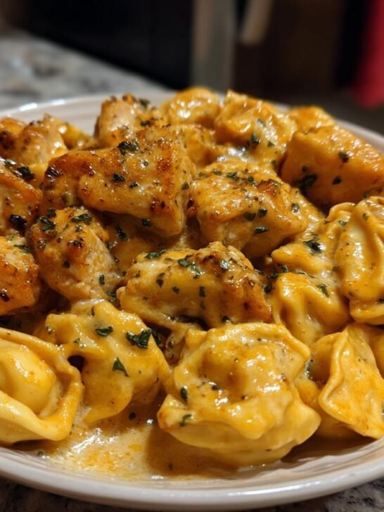 Close-up of creamy Garlic Butter Chicken Alfredo Tortellini topped with browned chicken pieces and parsley.