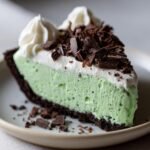 A decadent slice of Grasshopper Pie featuring a light green mint filling, chocolate crust, whipped cream, and chocolate shavings.