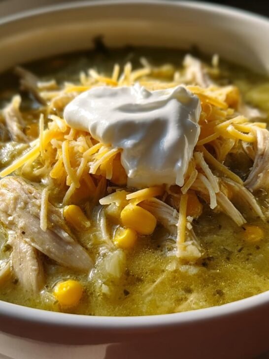 A close-up of a bowl of Green Chile Chicken Enchilada Soup topped with shredded cheese and sour cream.