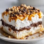 A decadent slice of the 4-layer Halloween Lush Recipe featuring whipped cream, chocolate, caramel drizzle, and nuts.