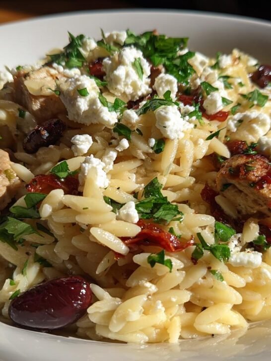 Close-up of High Protein Mediterranean Chicken Orzo topped with feta, olives, and parsley.