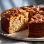 Close-up of a freshly baked, moist Spiced Apple Cake with a slice cut out, revealing tender apple pieces inside.