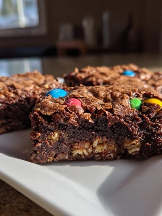 Close-up of fudgy Monster Cookie Fudgy Brownies squares topped with colorful M&Ms on a white plate.