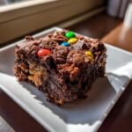 A close-up of a fudgy Monster Cookie Fudgy Brownies square topped with colorful candy-coated chocolates.