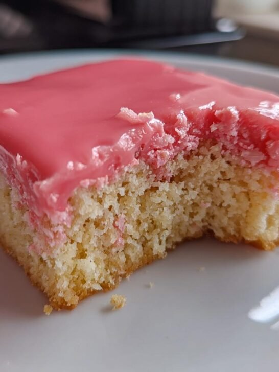 Close-up of a square slice of Pink Coconut Snowball Bars with bright pink icing and a bite taken out.