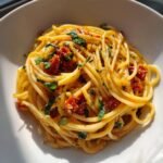 A close-up of a serving of Roasted Tomato Garlic Pasta tossed with sun-dried tomatoes and fresh basil leaves.