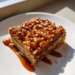A square of Salted Caramel Apple Crumble Bars topped with a generous drizzle of caramel sauce on a white plate.