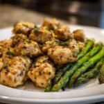 Close-up of seasoned chicken pieces and bright green asparagus on a white plate from Sheet Pan Lemon Chicken With Asparagus.