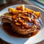 Close-up of a thick, bone-in smothered pork chops potatoes gravy served on a white plate.