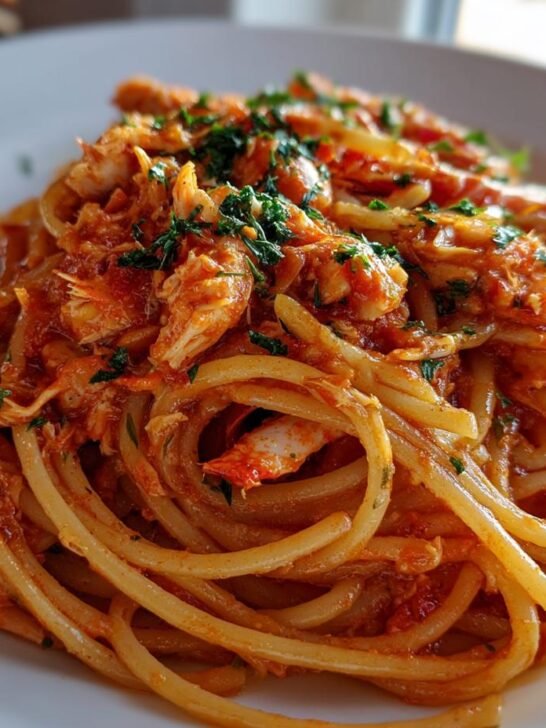 Close-up of a plate of Spicy Crab Pasta, featuring thick spaghetti tossed in a rich, reddish sauce with visible crab meat and fresh parsley.