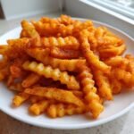 A plate piled high with crinkle-cut Zesty Louisiana Voodoo Fries, heavily coated in orange-red seasoning.